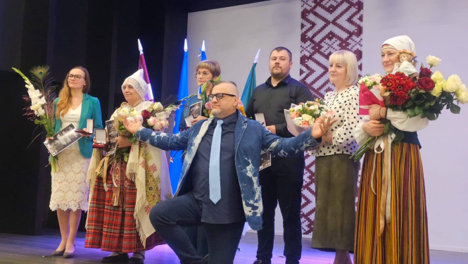 daudz cilvēki uz skatuves ar ziediem