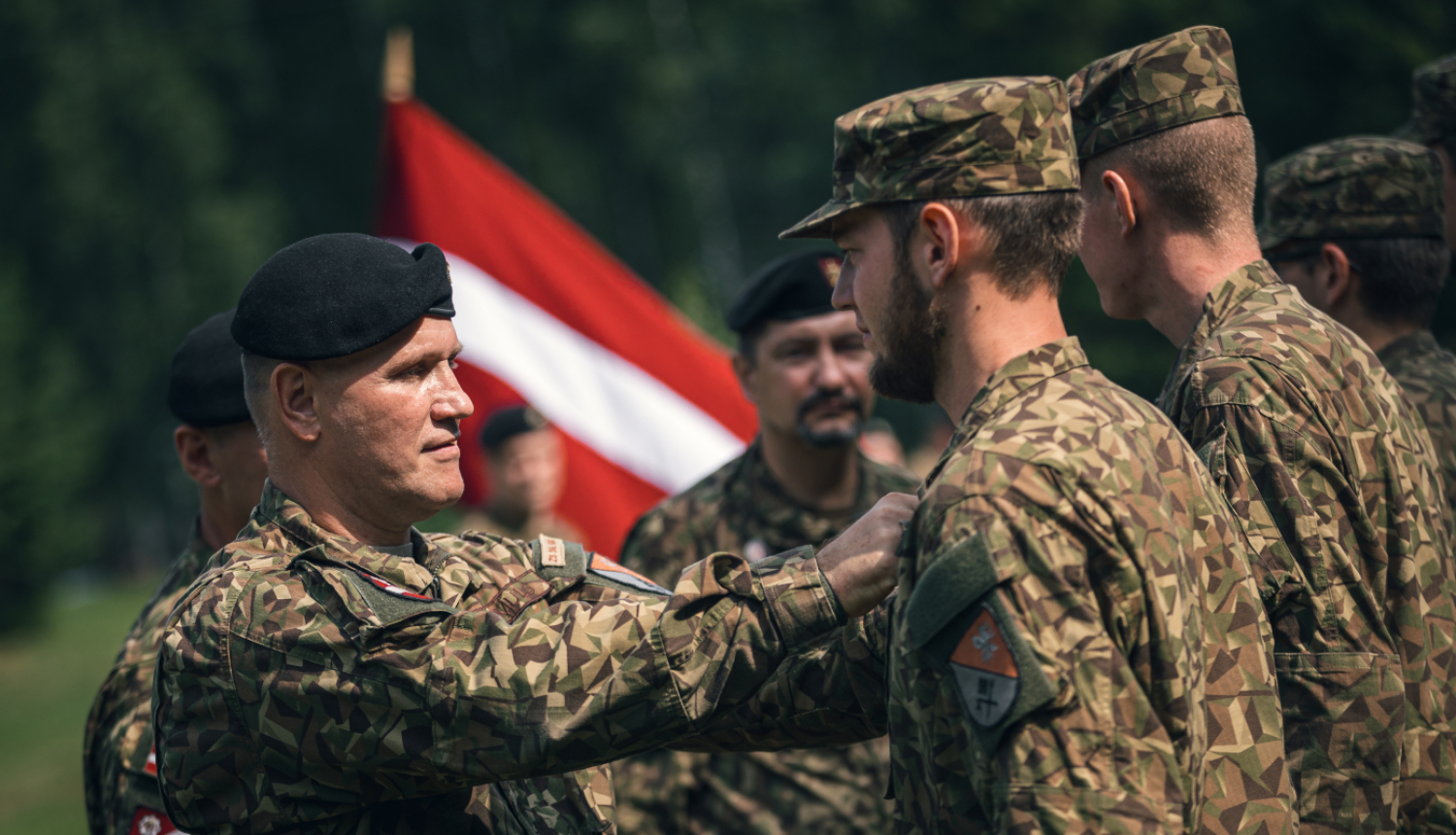 Cilvēki formastērpos, fonā plīvo Latvijas karogs