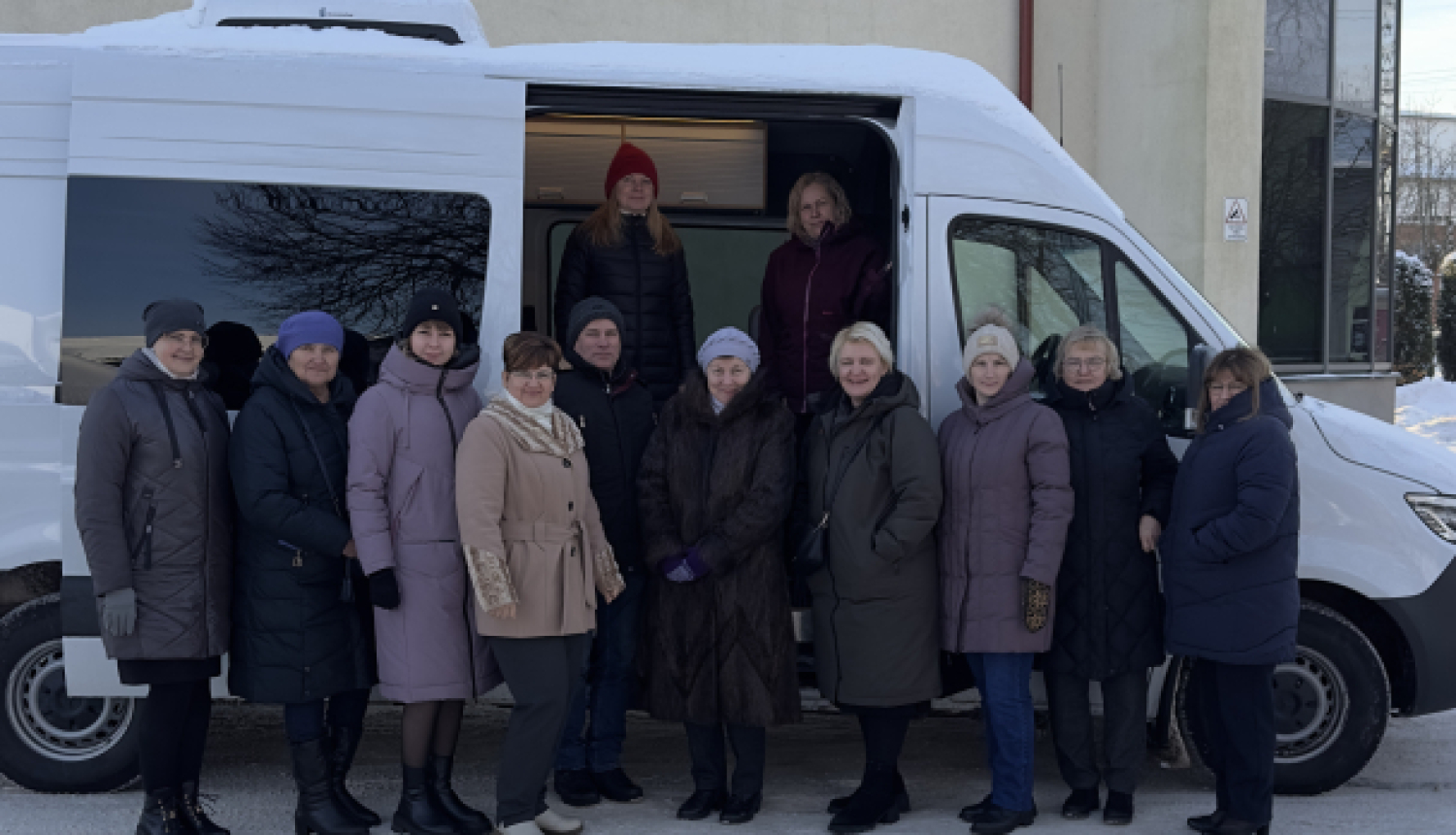 daudz cilvēku stāv pie balta busa