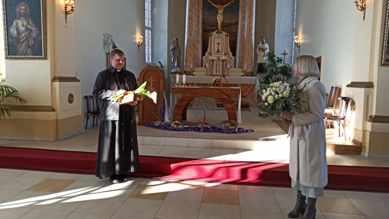 Skats no baznīcas - priesteris un sieviete ar ziediem