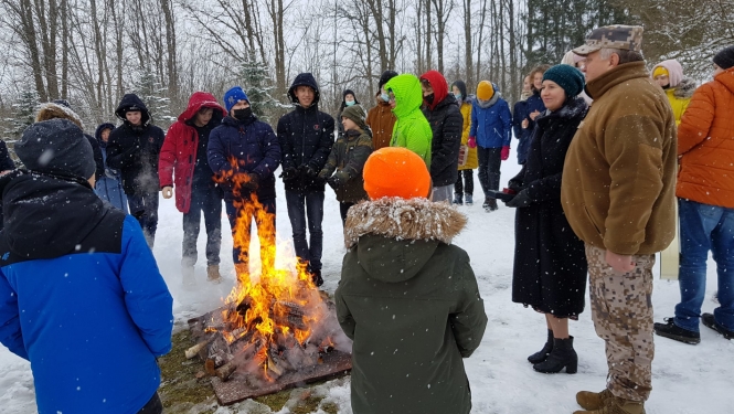 Bērni un divi pieaugušie stāv pie ugunskura ziemā