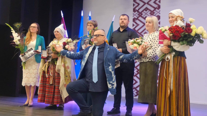 daudz cilvēki uz skatuves ar ziediem