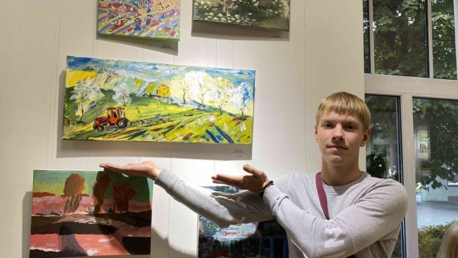 Zēns rāda uz savu gleznu pie sienas