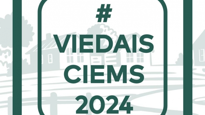 ciems fonā ar ēkām un pa virsu uzrakstīti burti - zaļš 