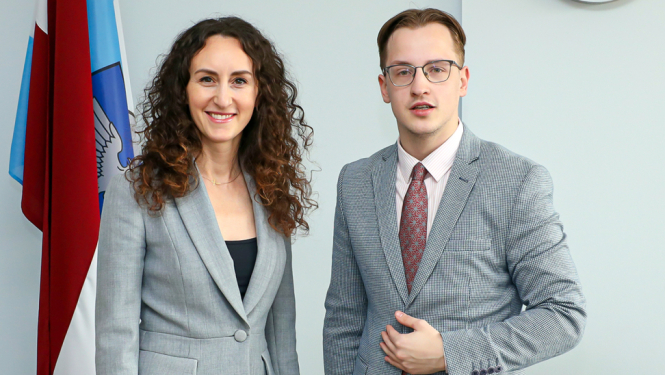 sieviete un vīrietis svinīgi pie karogiem pozē