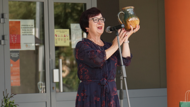 Sieviete ar māla krūzi rokās runā pie mikrofonā