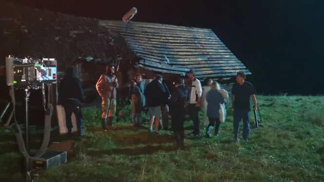 Filmas uzņemšana laukos - daudz cilvēku, fonā vecs šķūnis 