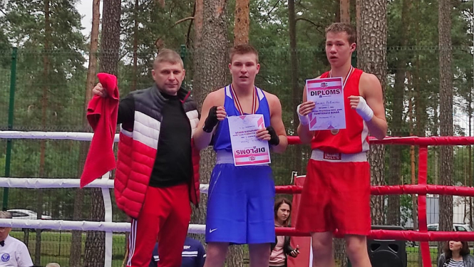 Trīs vīrieši stāv boksa ringā