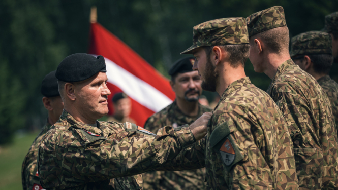 Cilvēki formastērpos, fonā plīvo Latvijas karogs