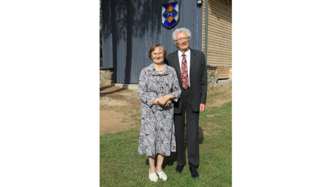 Vīrietis uzvalkā un sieviete kleitā stāv pie ēkas