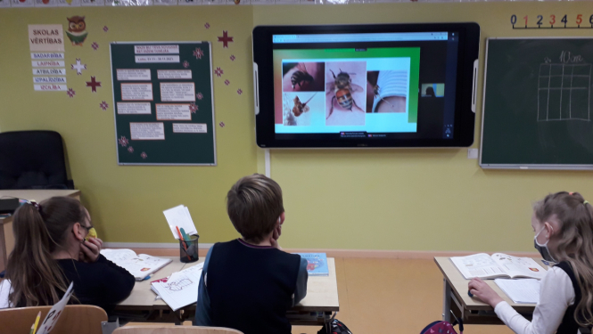 Bērni sēž solos un skatās prezentāciju