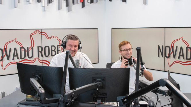 Divi vīrieši sēž radio studijā pie datoru monitoriem