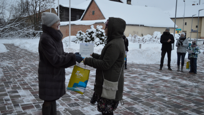 Sieviete meitenei pasniedz maisiņu un pateicības rakstu