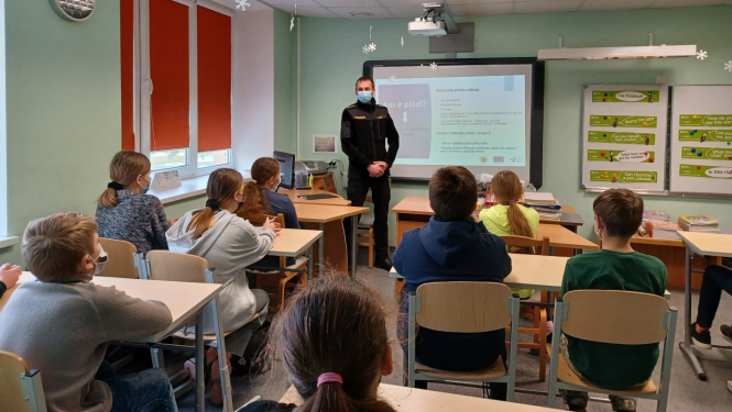 Ugunsdzēsējs stāv klases priekšā, bērni sēž solos