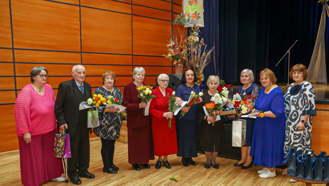 daudz cilvēku stāvrindā ar ziediem rokās