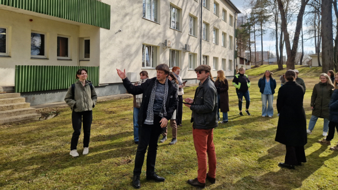 daudz cilvēku pie dzeltenas ēkas