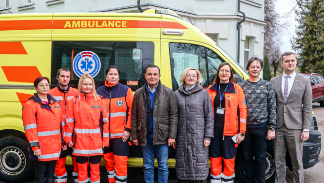 mediķi un politiķi stāv pie ātras palīdzības auto