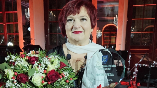 sieviete ar stikla balvu rokās un ziediem