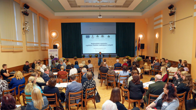 liela zāle pilna ar cilvēkiem, viens priekšā runā