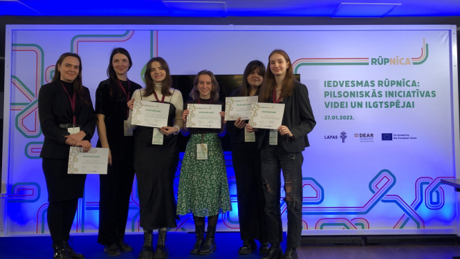 Vairāki cilvēki stāv ar diplomiem rokās