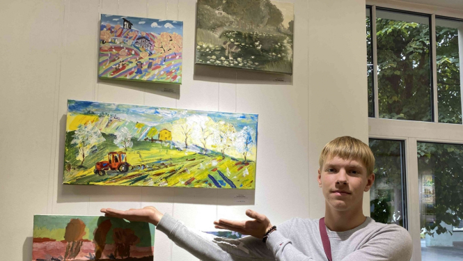 Zēns rāda uz savu gleznu pie sienas