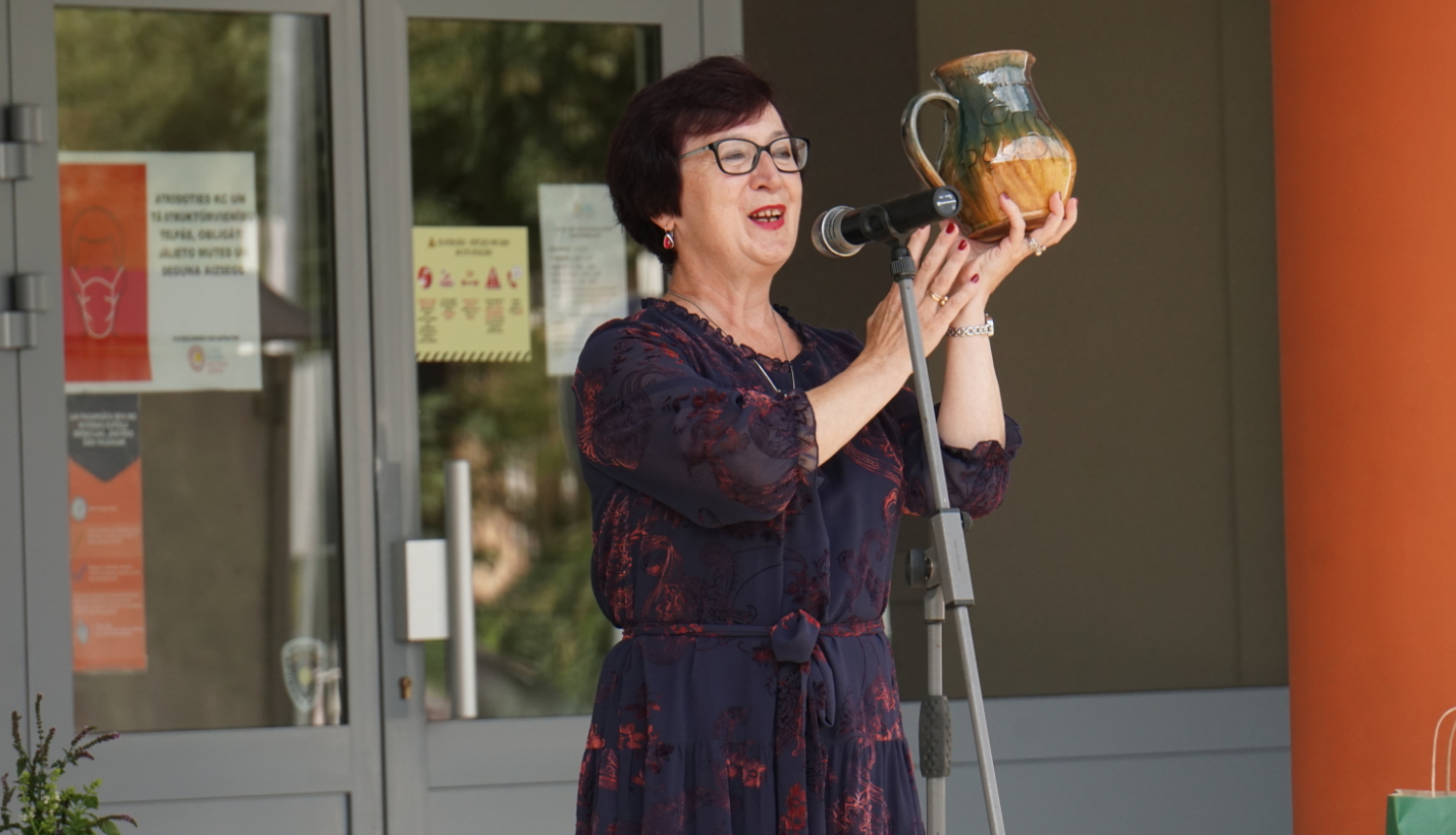 Sieviete ar māla krūzi rokās runā pie mikrofonā