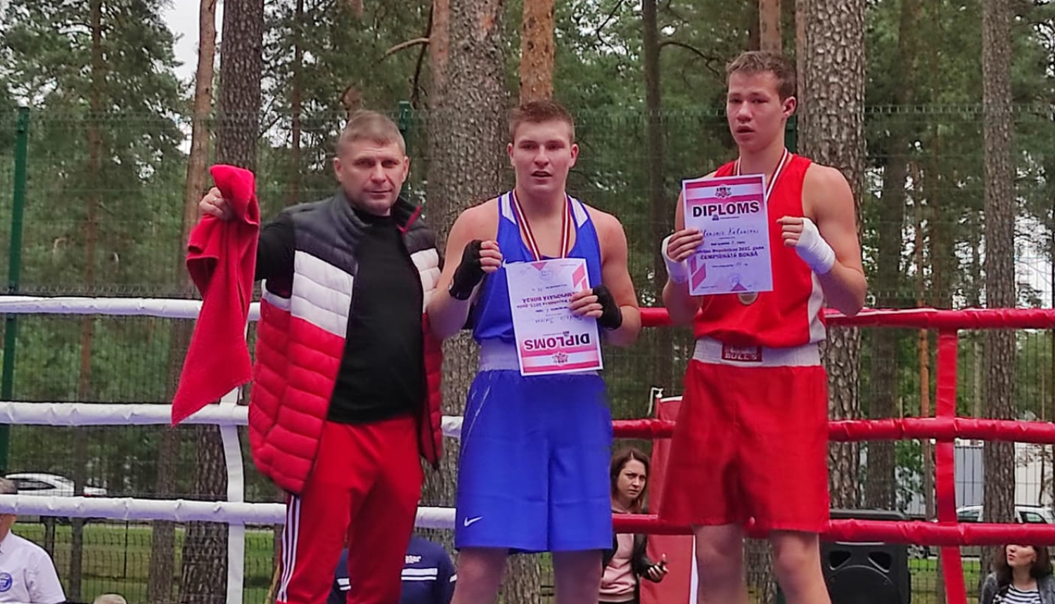 Trīs vīrieši stāv boksa ringā