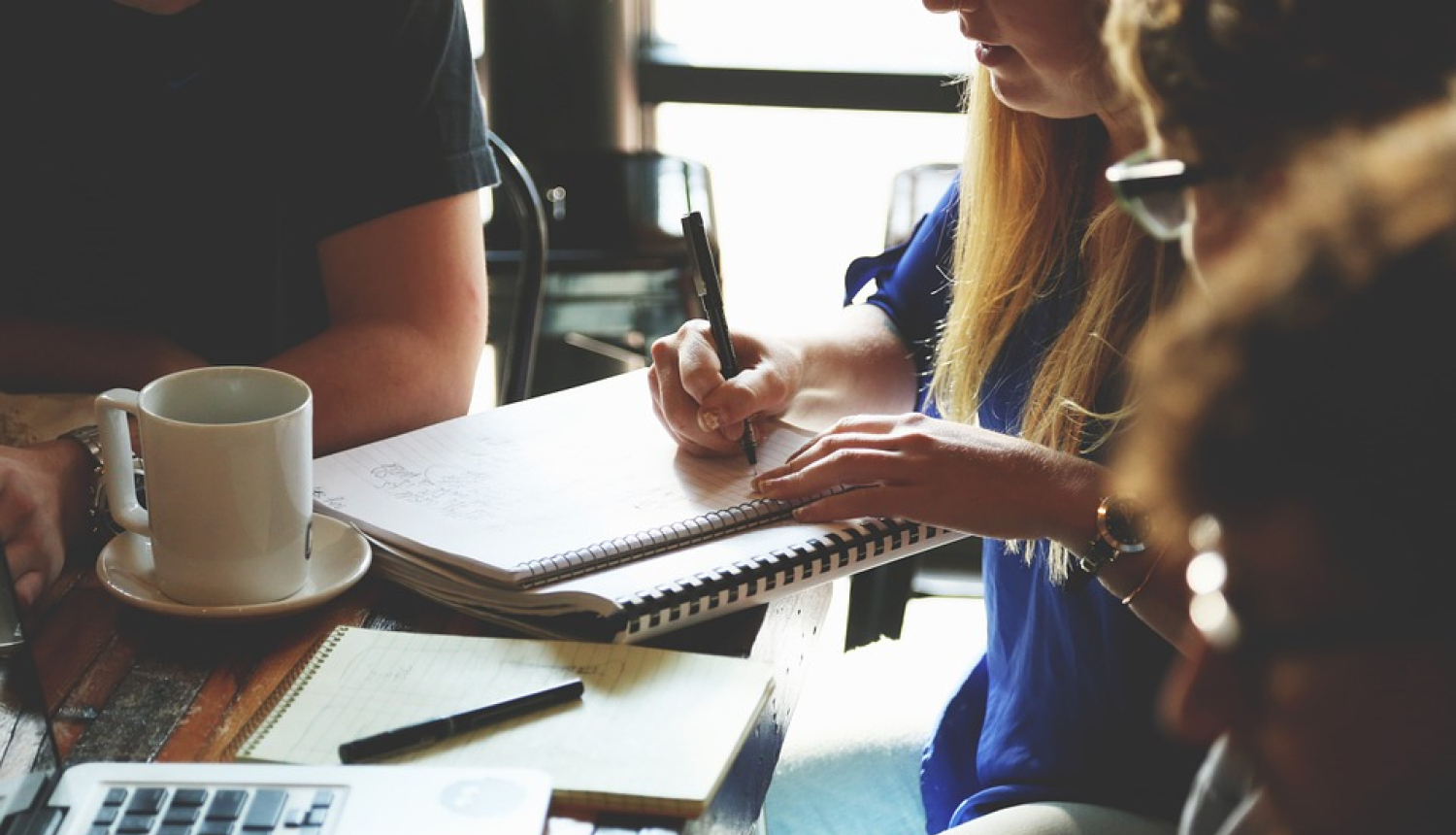 Cilvēki pie galda veic piezīmes bloknotā