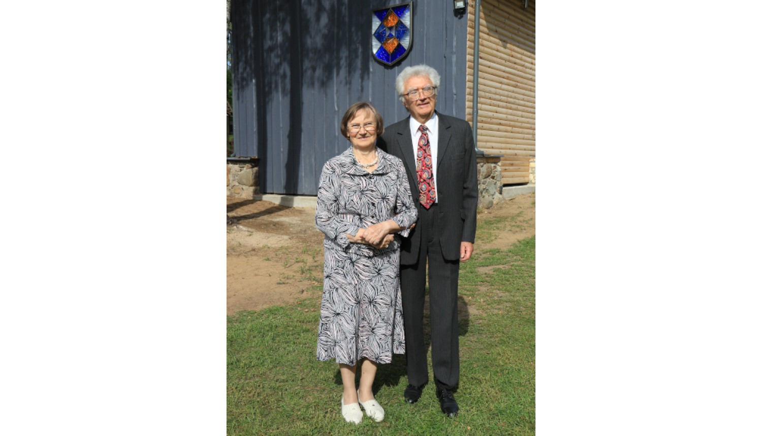 Vīrietis uzvalkā un sieviete kleitā stāv pie ēkas