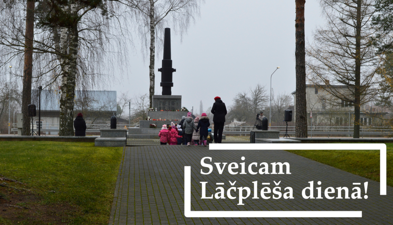 Bērnu grupiņa pa ietvi dodas pie pieminekļa