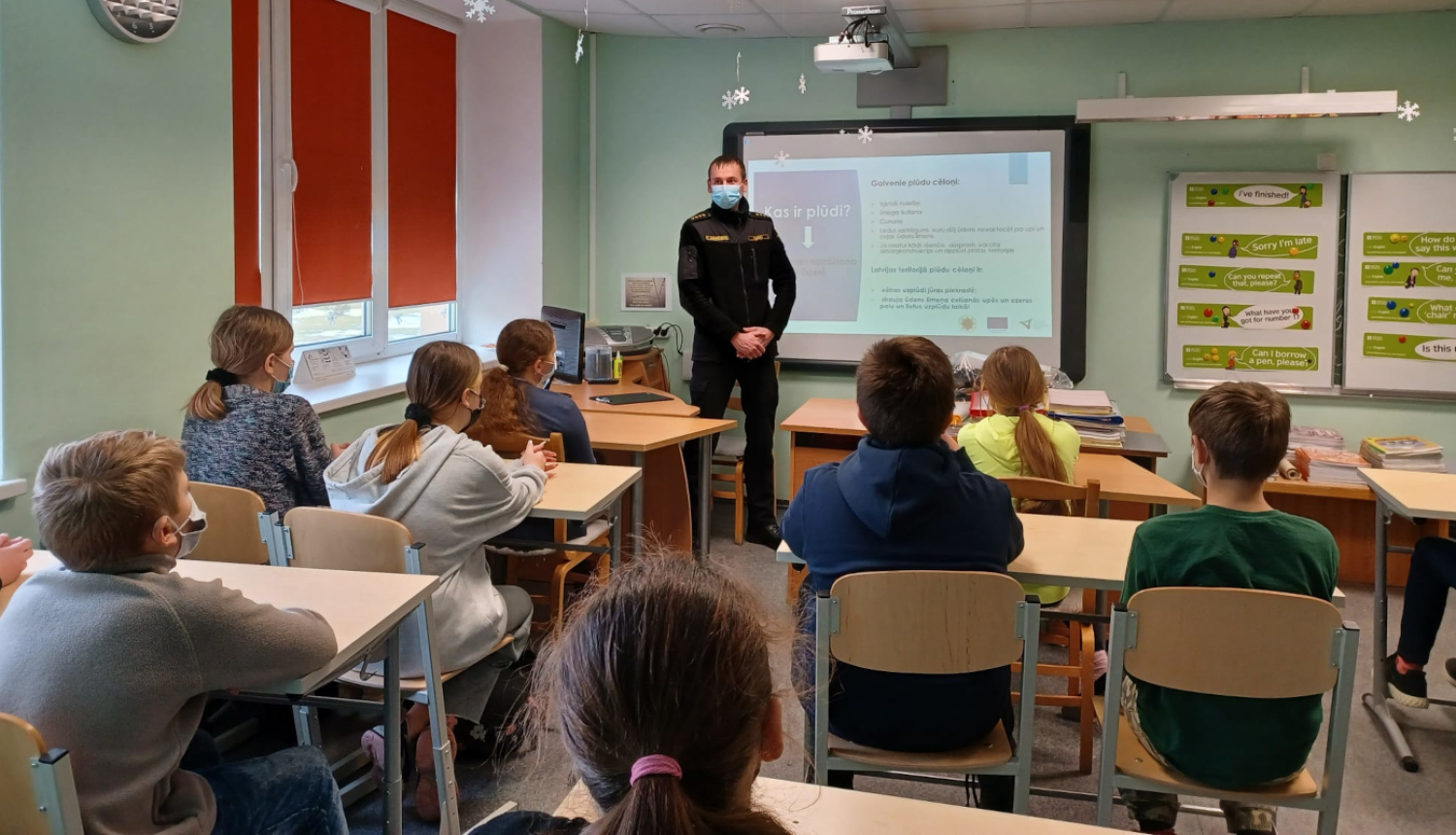 Ugunsdzēsējs stāv klases priekšā, bērni sēž solos