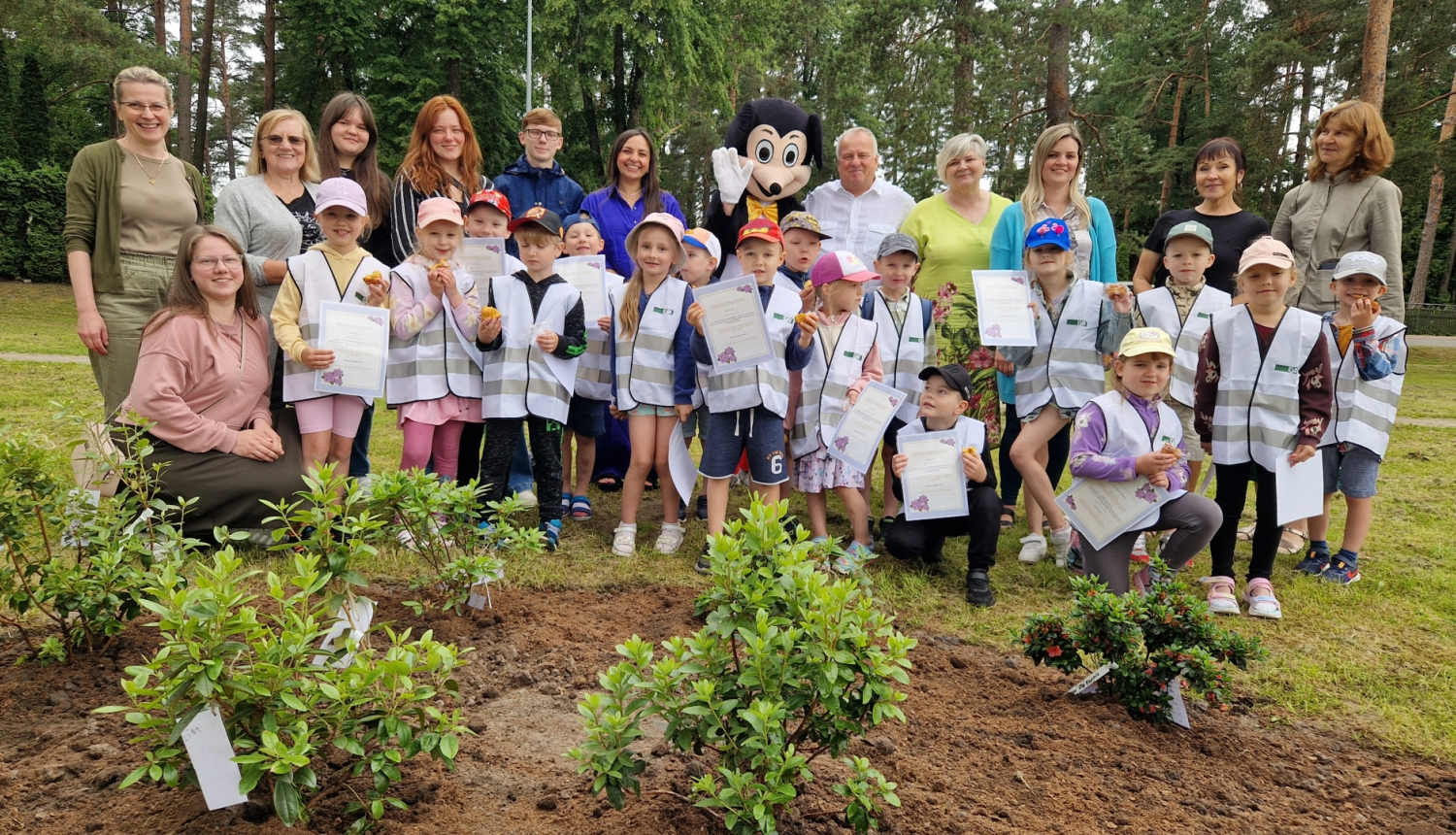 bērni kopā ar mikipeli ārā parkā stāv