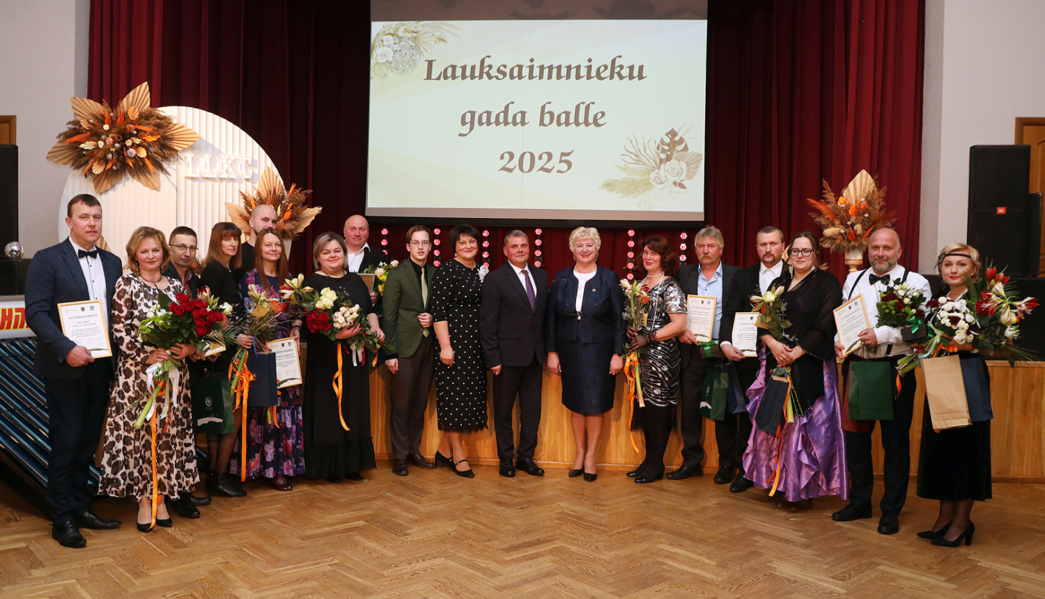 daudz cilvēki svinīgi stāv ar ziediem