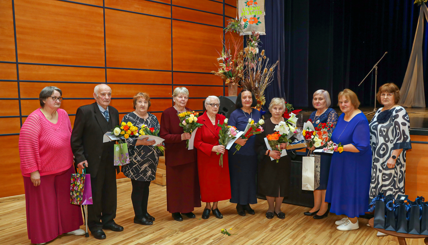 daudz cilvēku stāvrindā ar ziediem rokās