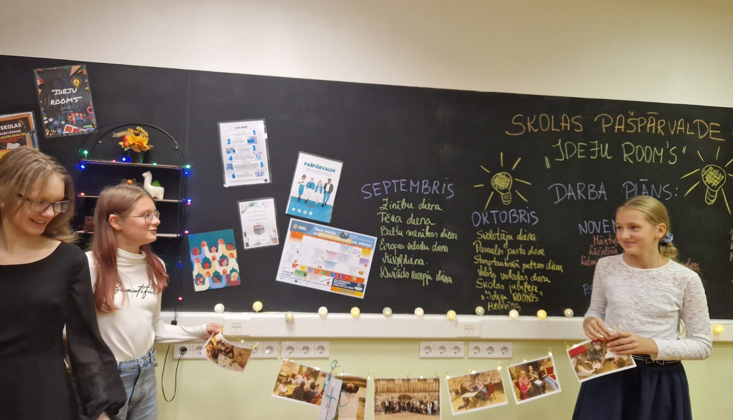 trīs meitenes stāv pie tāfeles