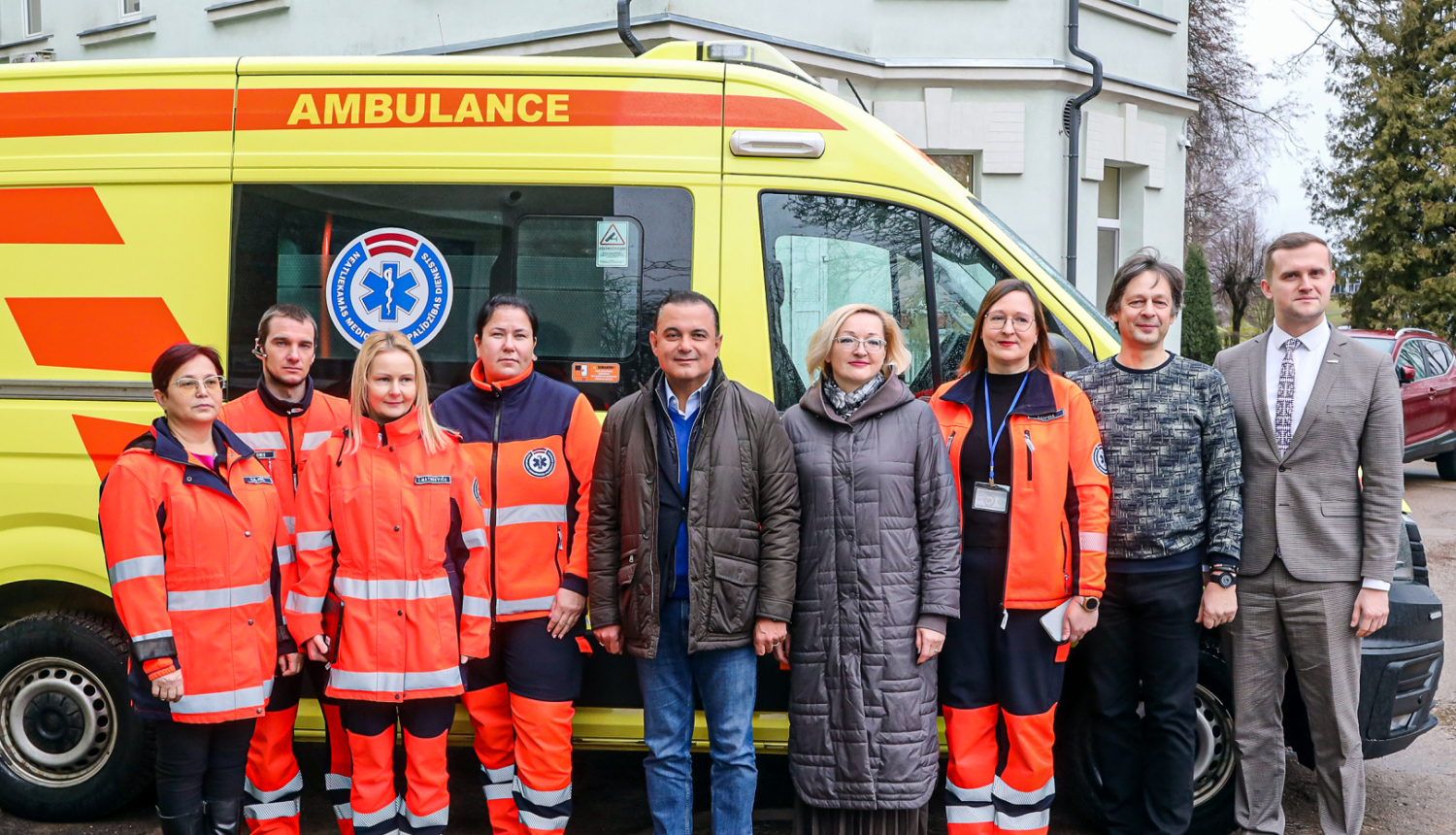 mediķi un politiķi stāv pie ātras palīdzības auto
