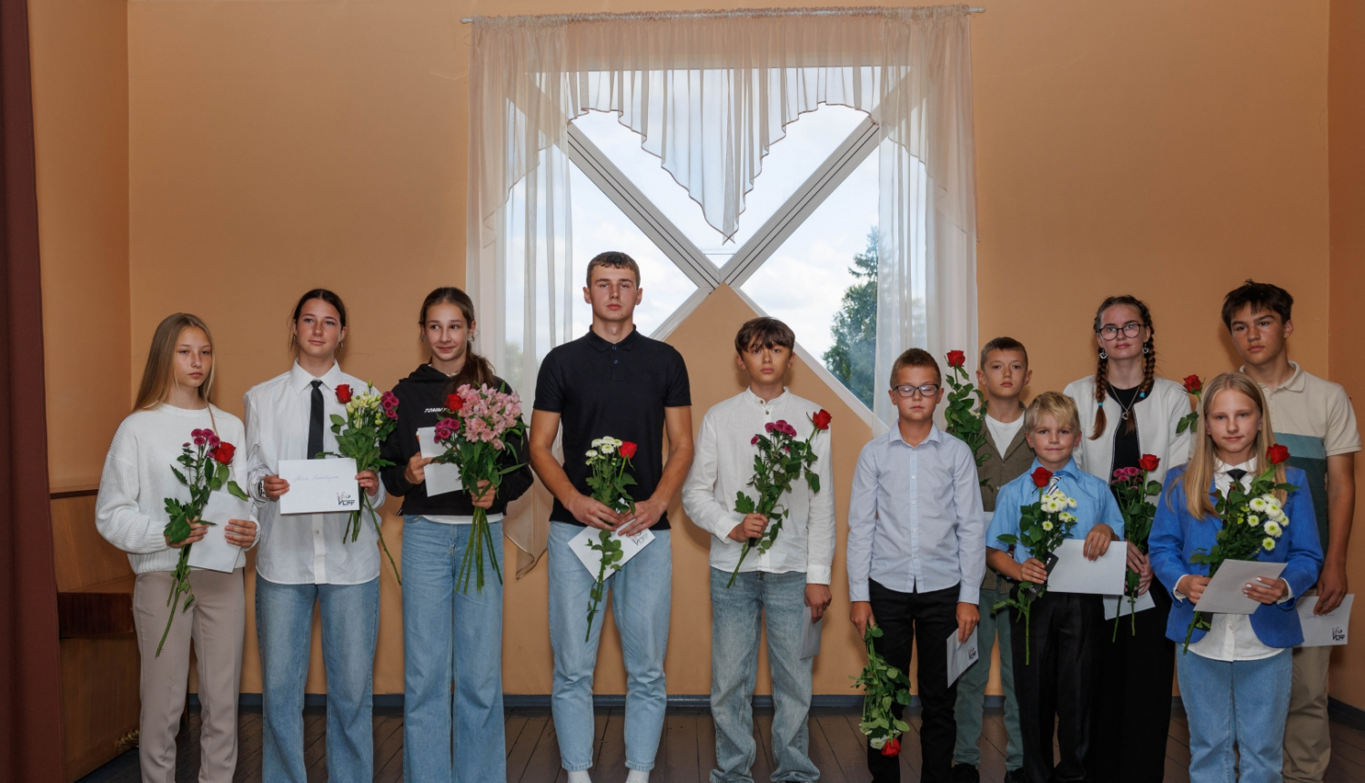 bērni stāv rindā ar ziediem un aploksnēm