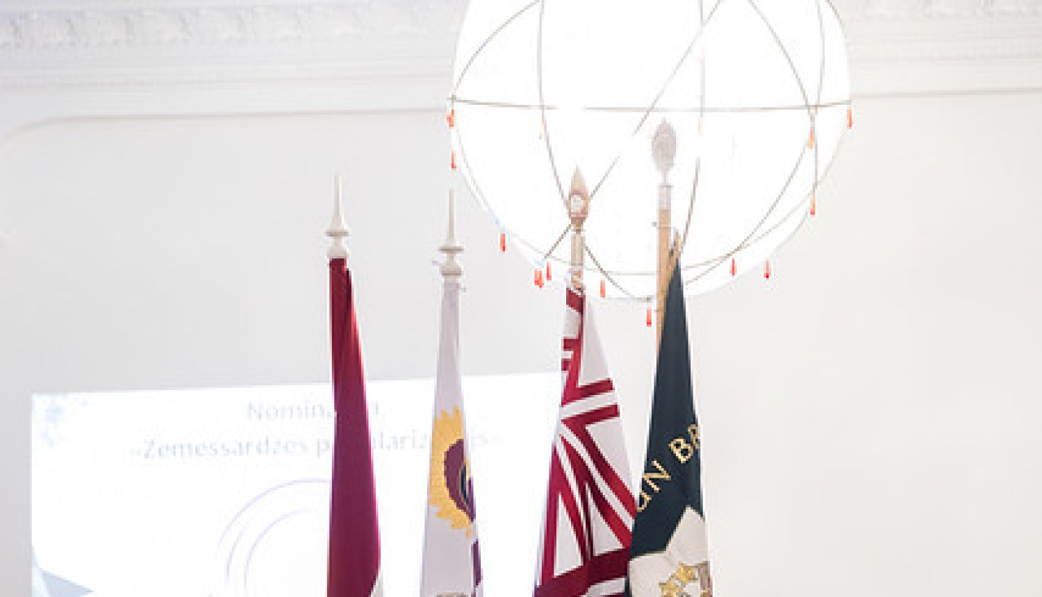 pie valsts karoga stāv sieviete un 3 vīrieši formas tērpos