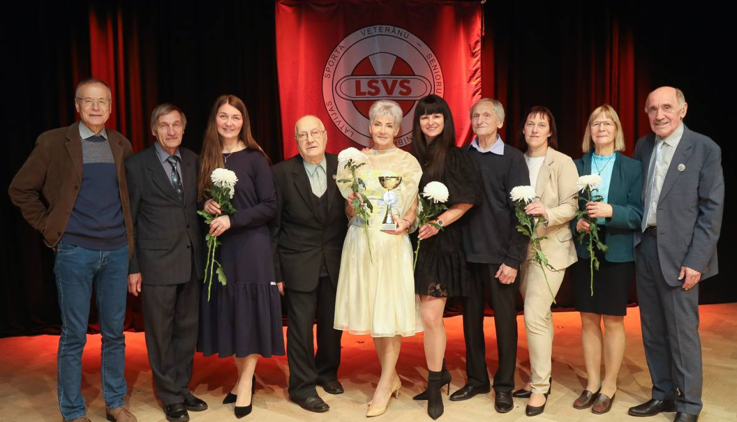 daudz cilvēku stāv uz skatuves