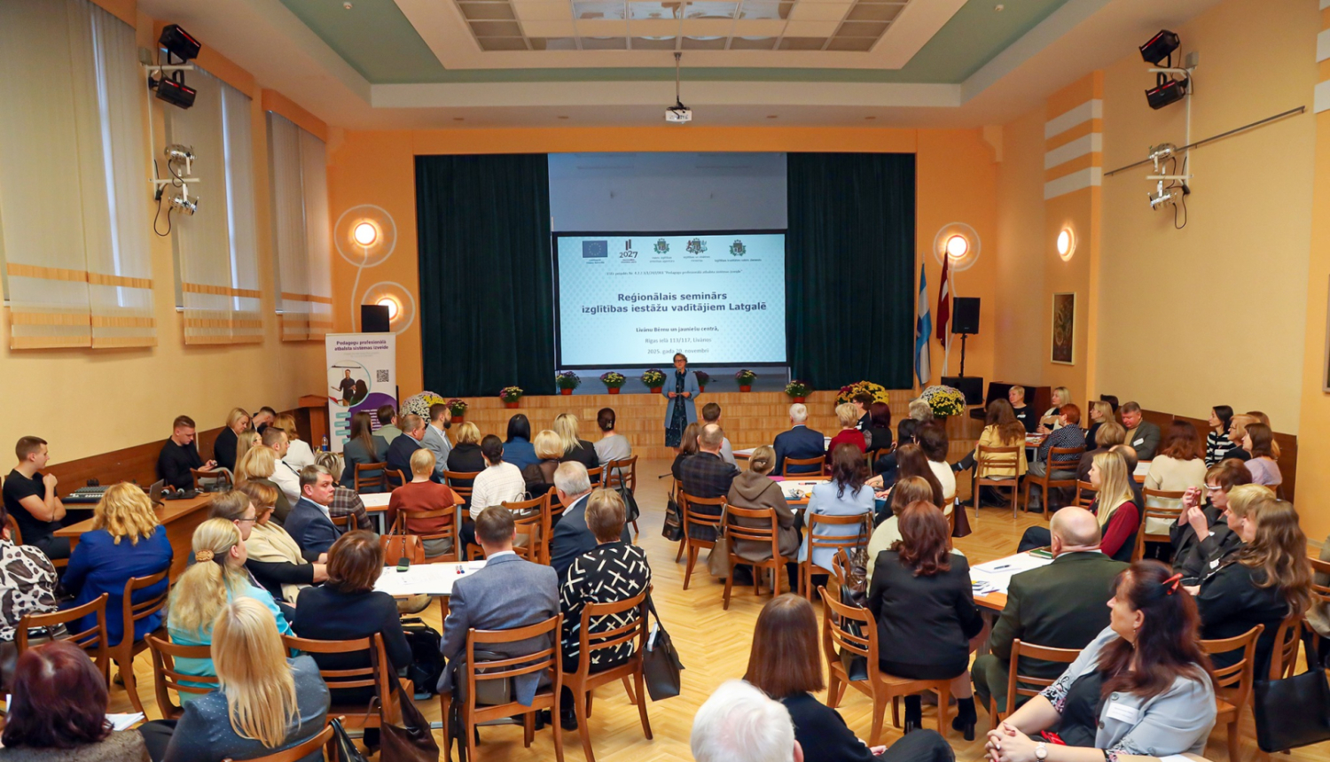 liela zāle pilna ar cilvēkiem, viens priekšā runā