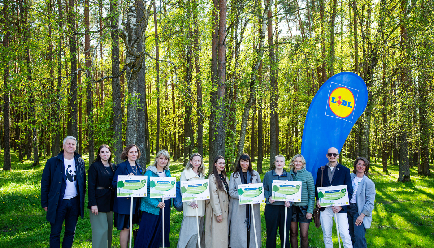 daudz cilvēki stāv ar plakātiem dabā pie meža