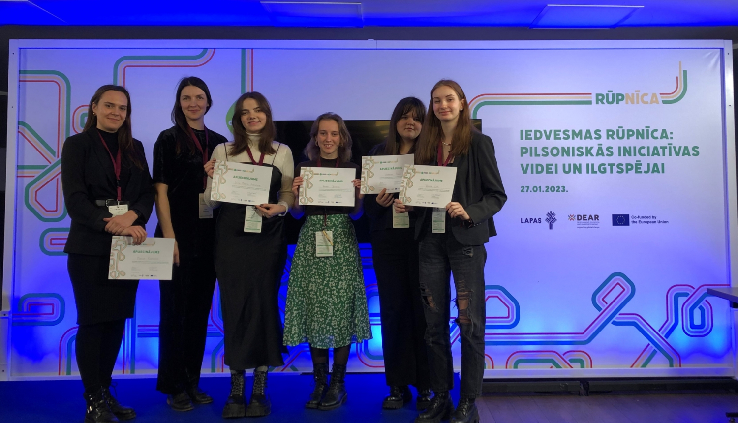 Vairāki cilvēki stāv ar diplomiem rokās