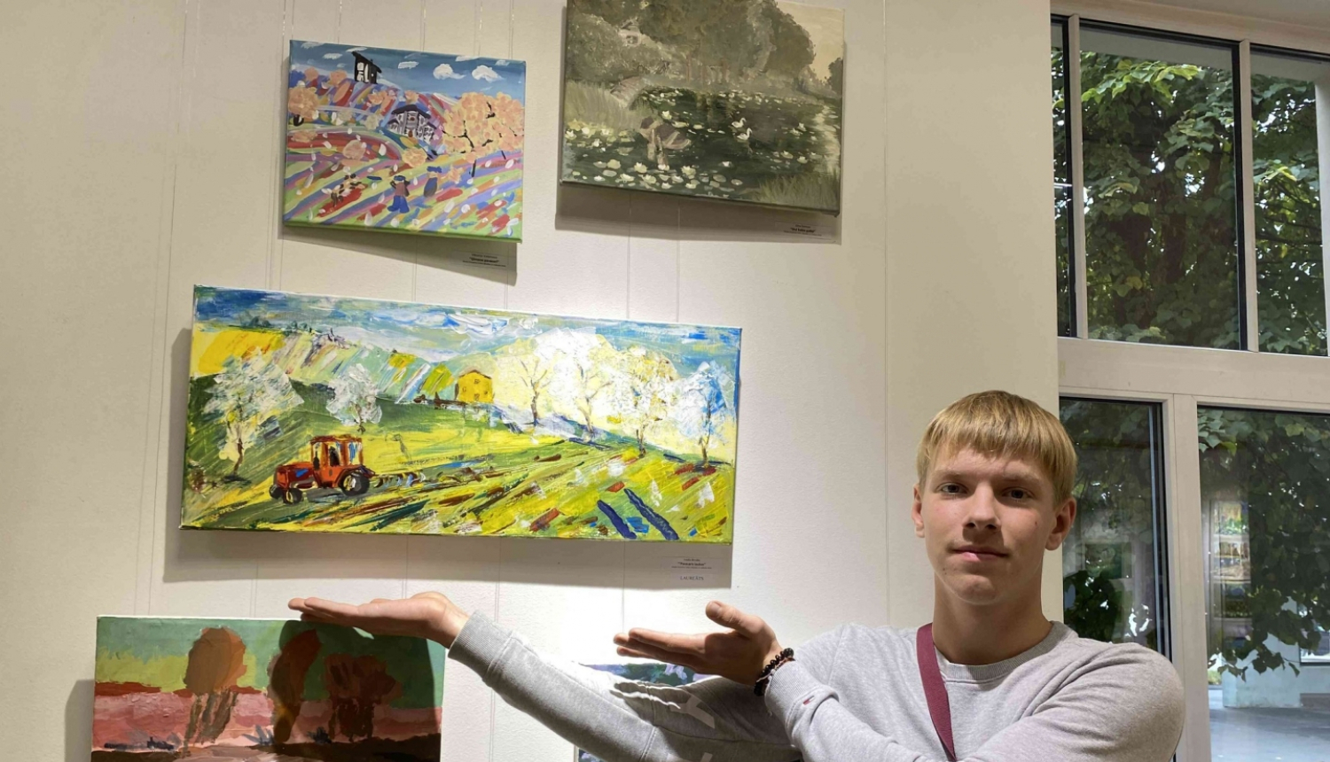 Zēns rāda uz savu gleznu pie sienas