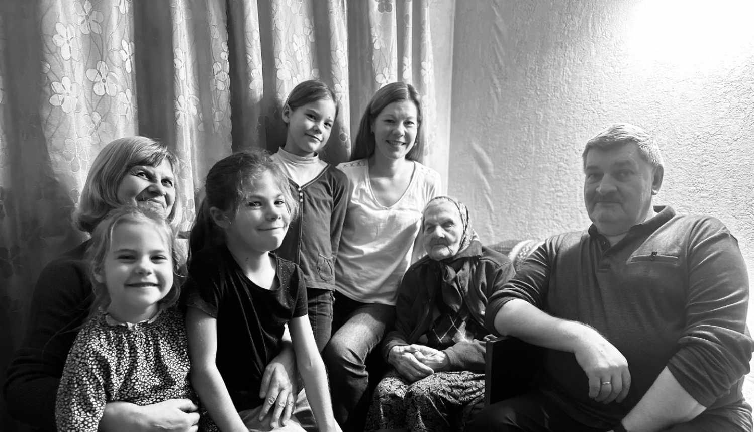 daudz cilvēku sēž ar sirmu kundzi