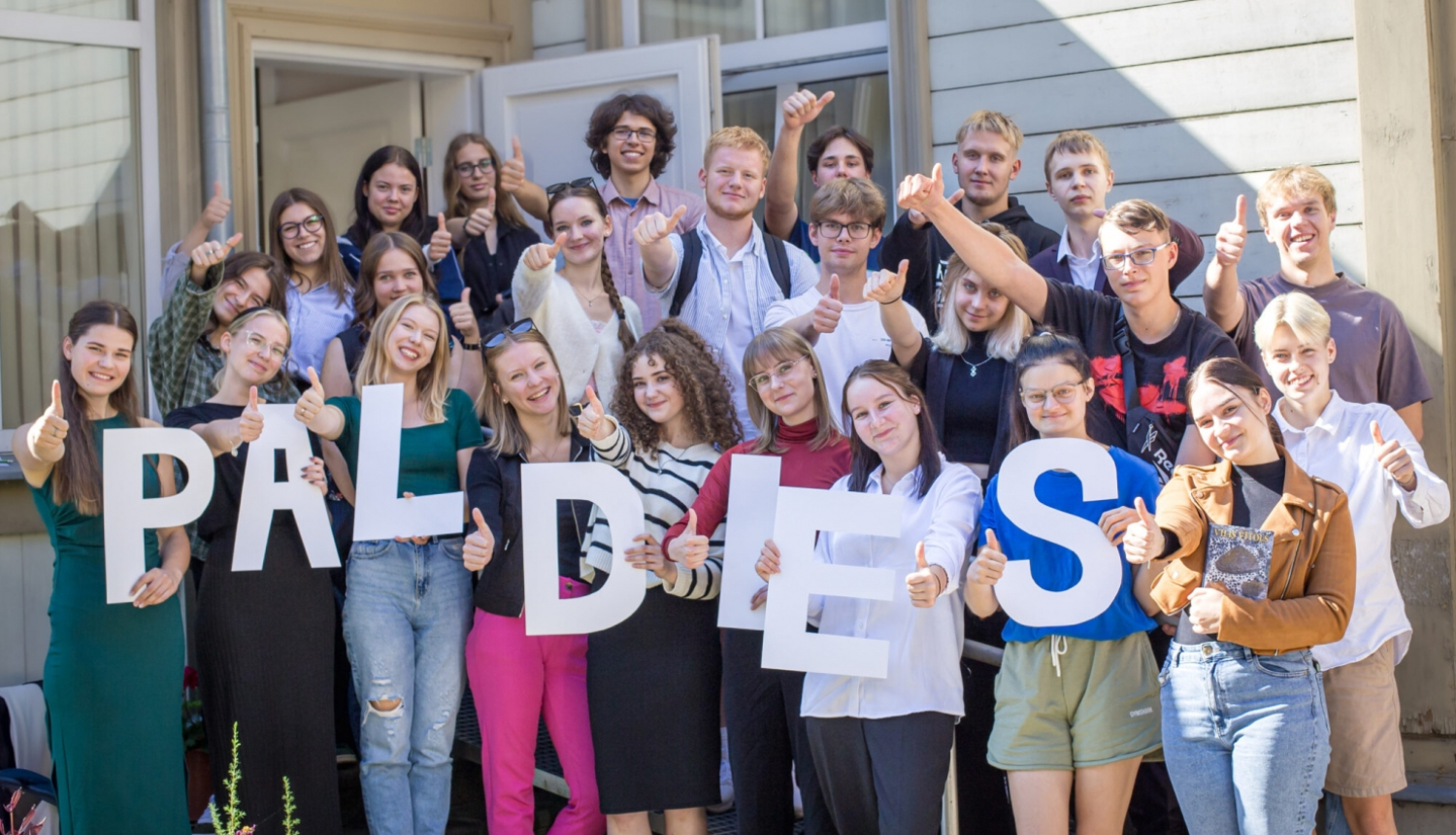 Jaunieši stāv uz trepēm, turot rokās uzrakstu "Paldies"