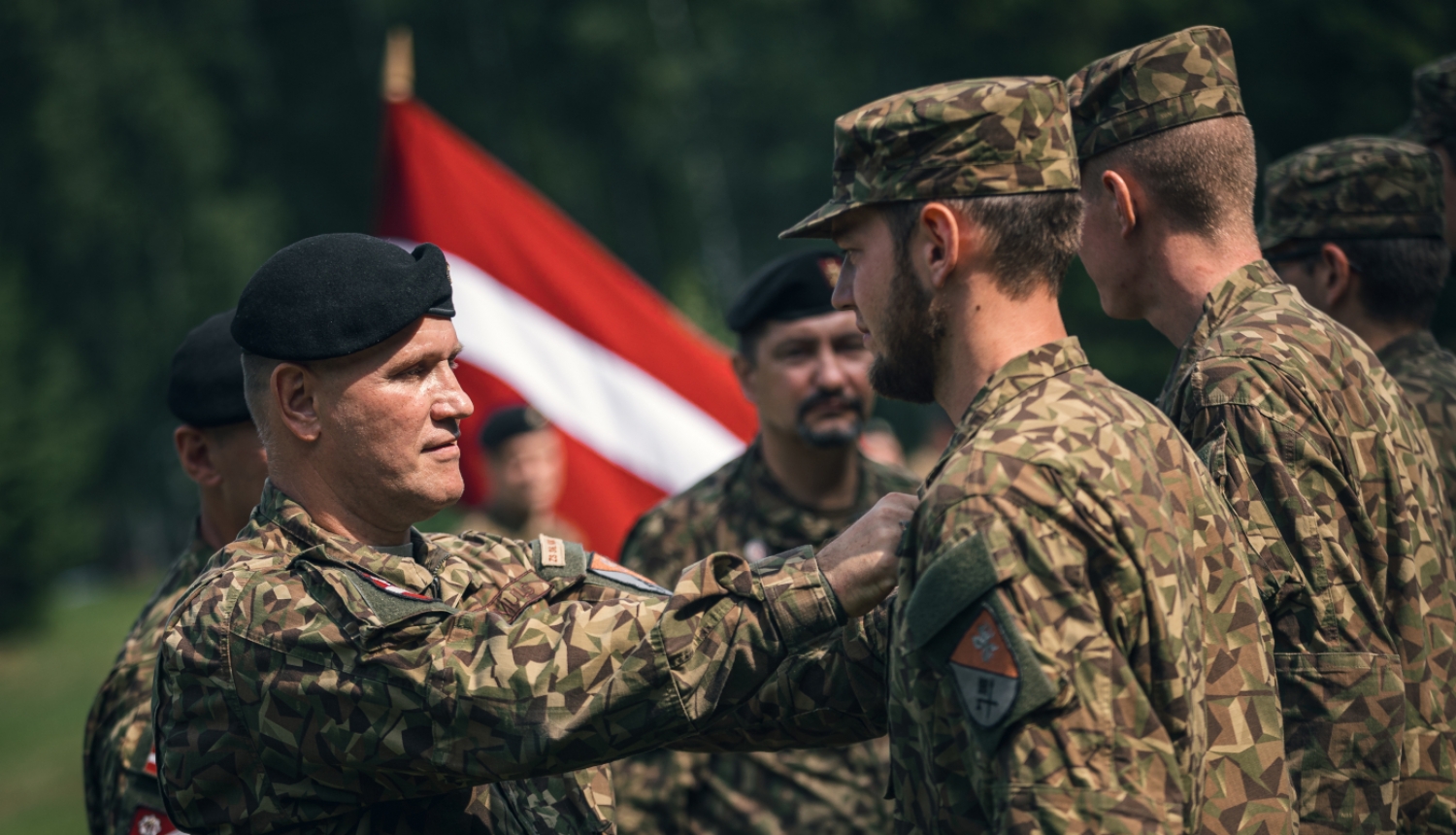 Cilvēki formastērpos, fonā plīvo Latvijas karogs