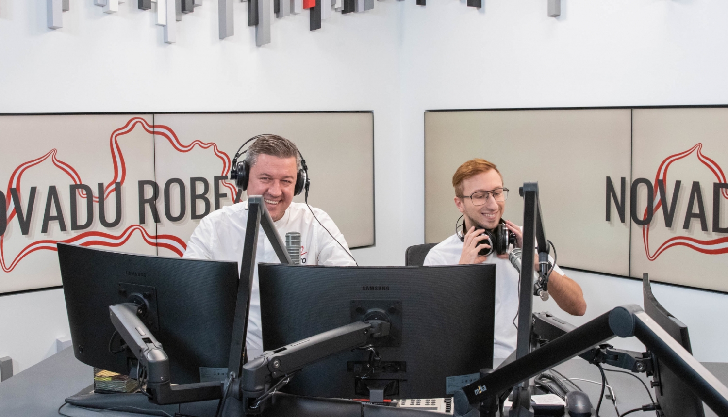 Divi vīrieši sēž radio studijā pie datoru monitoriem