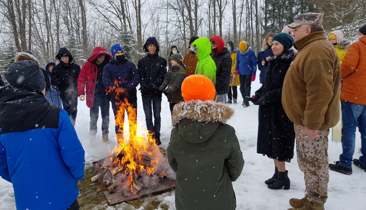 Bērni un divi pieaugušie stāv pie ugunskura ziemā