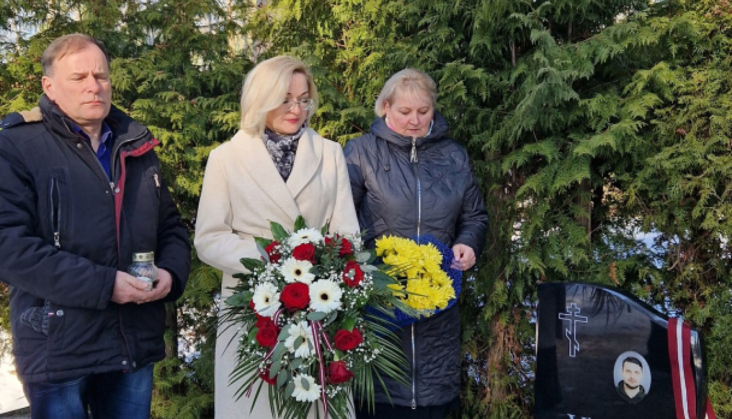 trīs cilveki pie kapavietas