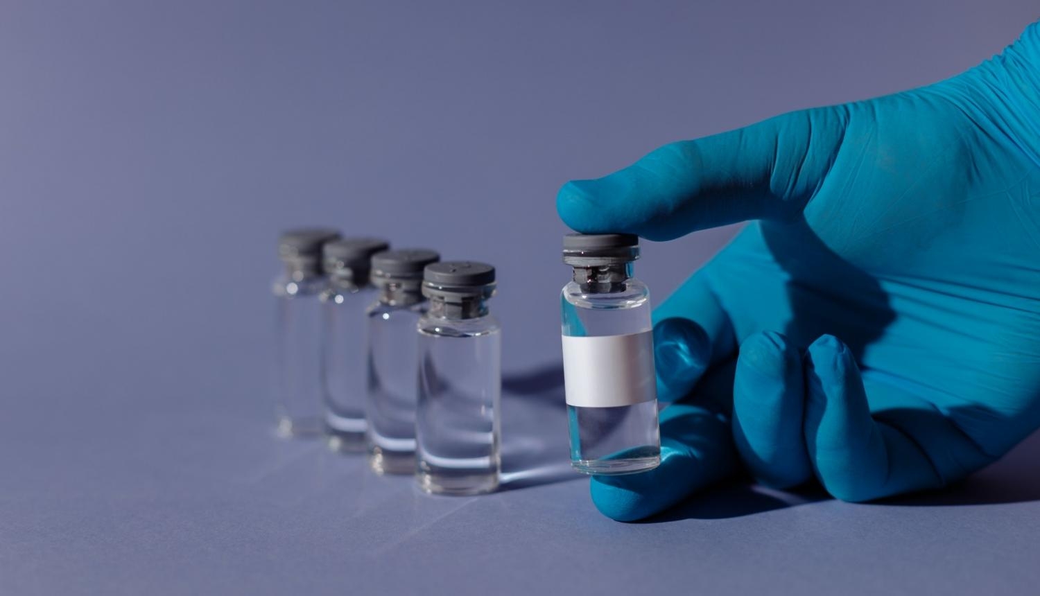 Vakcīnas pudelītes un cilvēka roka